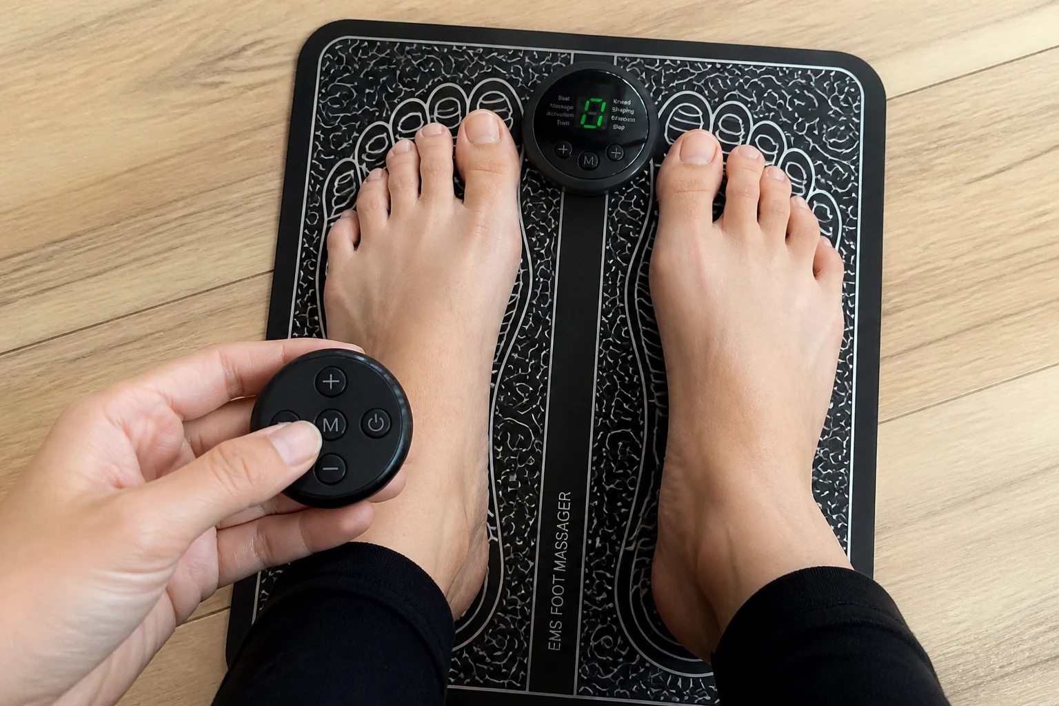 Bare feet aligned on an EMS foot massager mat while adjusting the wireless remote